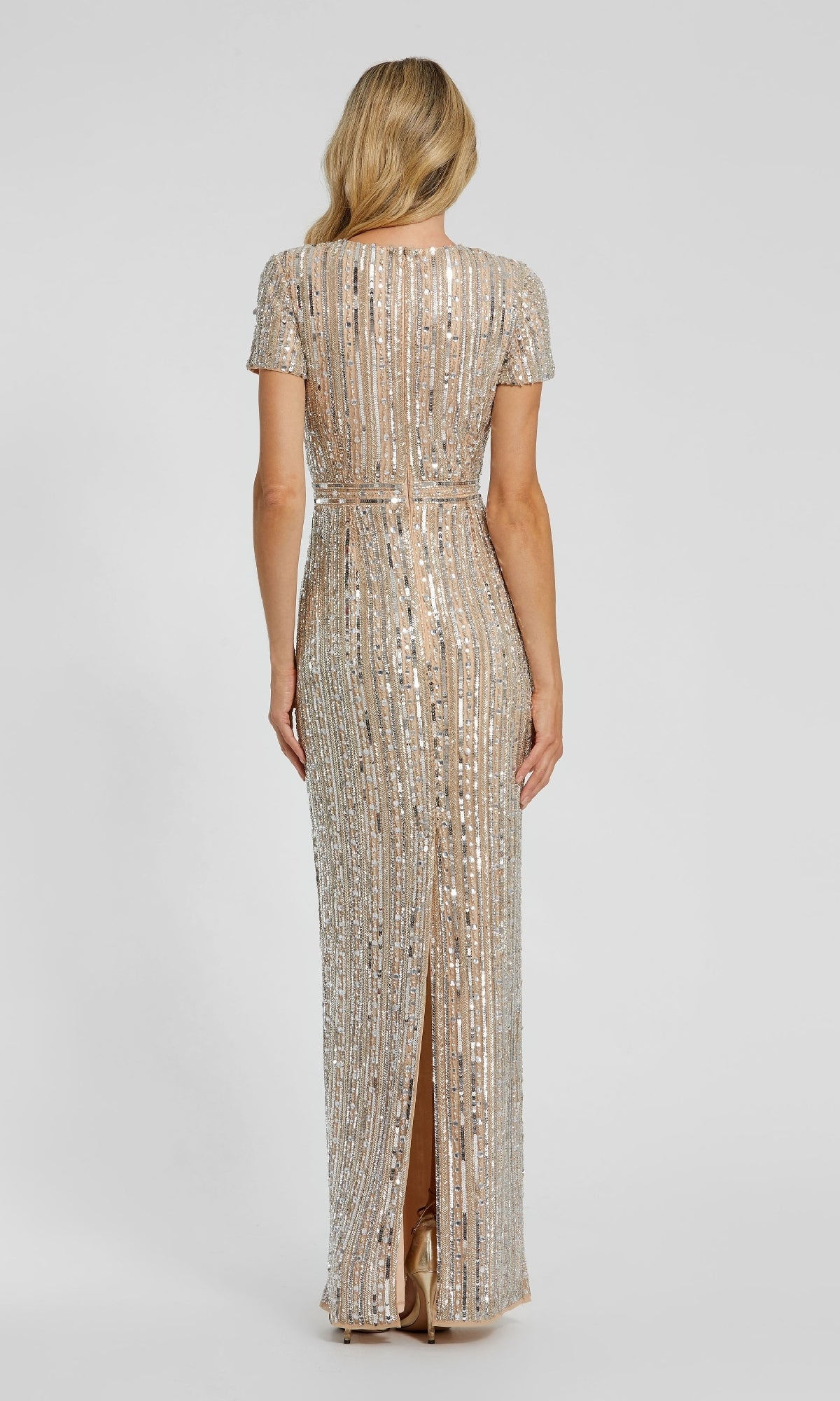 A woman with long blonde hair is seen from the back wearing the Mac Duggal 93829, a floor-length gold sequin formal dress with short sleeves and vertical stripes.